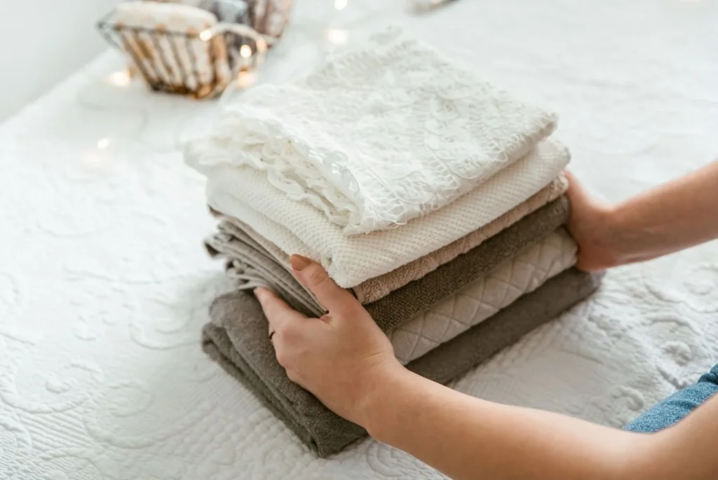 Person arranging neatly folded neutral-colored towels on a white textured surface, emphasizing home organization and decluttering.