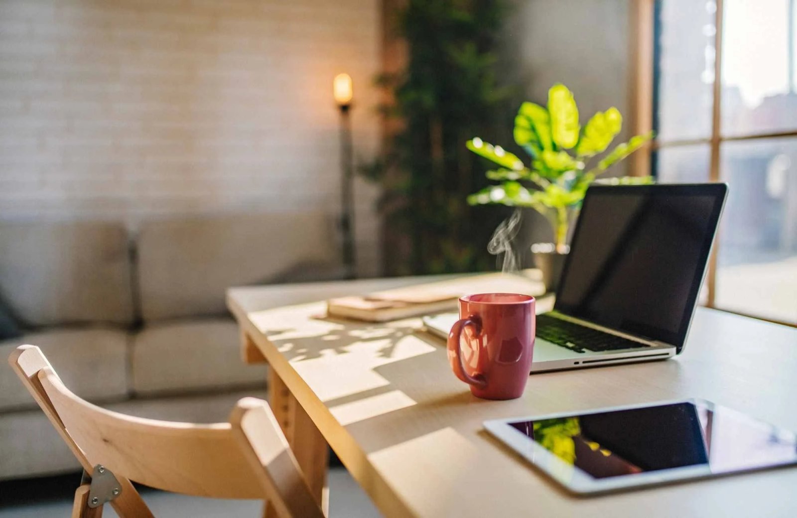 Modern minimalist home office setup with laptop, steaming coffee mug, and green plant, emphasizing productivity and organization for remote work.